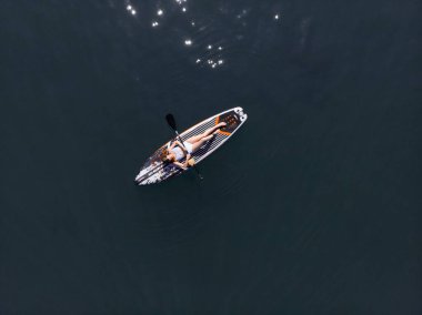 Stand Up Paddle tahtasında çekici bir kadın yemek masasında kürek çeken ve şeffaf suyun tadını çıkaran bir kadın. Tropik seyahat, seyahat tutkusu ve su aktivitesi konsepti. Gün batımı ve rahatlama