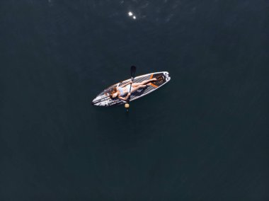 Stand Up Paddle tahtasında çekici bir kadın yemek masasında kürek çeken ve şeffaf suyun tadını çıkaran bir kadın. Tropik seyahat, seyahat tutkusu ve su aktivitesi konsepti. Gün batımı ve rahatlama
