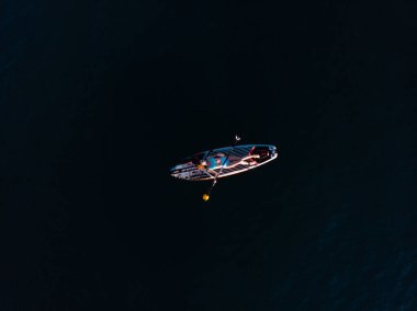 Stand Up Paddle tahtasında çekici bir kadın yemek masasında kürek çeken ve şeffaf suyun tadını çıkaran bir kadın. Tropik seyahat, seyahat tutkusu ve su aktivitesi konsepti. Gün batımı ve rahatlama