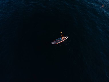 Stand Up Paddle tahtasında çekici bir kadın yemek masasında kürek çeken ve şeffaf suyun tadını çıkaran bir kadın. Tropik seyahat, seyahat tutkusu ve su aktivitesi konsepti. Gün batımı ve rahatlama