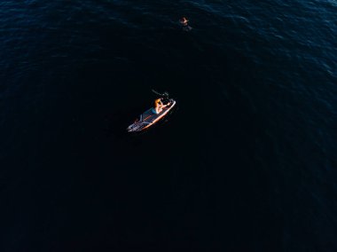 Stand Up Paddle tahtasında çekici bir kadın yemek masasında kürek çeken ve şeffaf suyun tadını çıkaran bir kadın. Tropik seyahat, seyahat tutkusu ve su aktivitesi konsepti. Gün batımı ve rahatlama