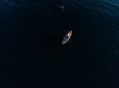 Stand Up Paddle tahtasında çekici bir kadın yemek masasında kürek çeken ve şeffaf suyun tadını çıkaran bir kadın. Tropik seyahat, seyahat tutkusu ve su aktivitesi konsepti. Gün batımı ve rahatlama