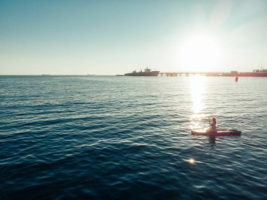 Stand Up Paddle tahtasında çekici bir kadın yemek masasında kürek çeken ve şeffaf suyun tadını çıkaran bir kadın. Tropik seyahat, seyahat tutkusu ve su aktivitesi konsepti. Gün batımı ve rahatlama
