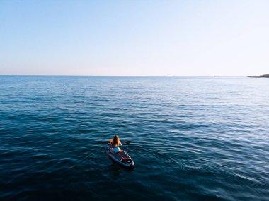 Stand Up Paddle tahtasında çekici bir kadın yemek masasında kürek çeken ve şeffaf suyun tadını çıkaran bir kadın. Tropik seyahat, seyahat tutkusu ve su aktivitesi konsepti. Gün batımı ve rahatlama