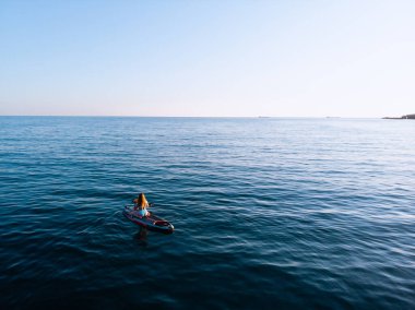 Stand Up Paddle tahtasında çekici bir kadın yemek masasında kürek çeken ve şeffaf suyun tadını çıkaran bir kadın. Tropik seyahat, seyahat tutkusu ve su aktivitesi konsepti. Gün batımı ve rahatlama