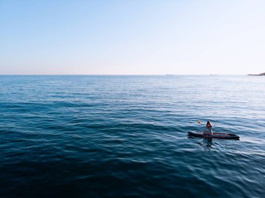 Stand Up Paddle tahtasında çekici bir kadın yemek masasında kürek çeken ve şeffaf suyun tadını çıkaran bir kadın. Tropik seyahat, seyahat tutkusu ve su aktivitesi konsepti. Gün batımı ve rahatlama