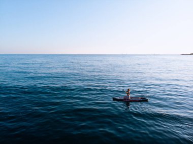 Stand Up Paddle tahtasında çekici bir kadın yemek masasında kürek çeken ve şeffaf suyun tadını çıkaran bir kadın. Tropik seyahat, seyahat tutkusu ve su aktivitesi konsepti. Gün batımı ve rahatlama