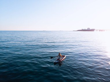 Stand Up Paddle tahtasında çekici bir kadın yemek masasında kürek çeken ve şeffaf suyun tadını çıkaran bir kadın. Tropik seyahat, seyahat tutkusu ve su aktivitesi konsepti. Gün batımı ve rahatlama