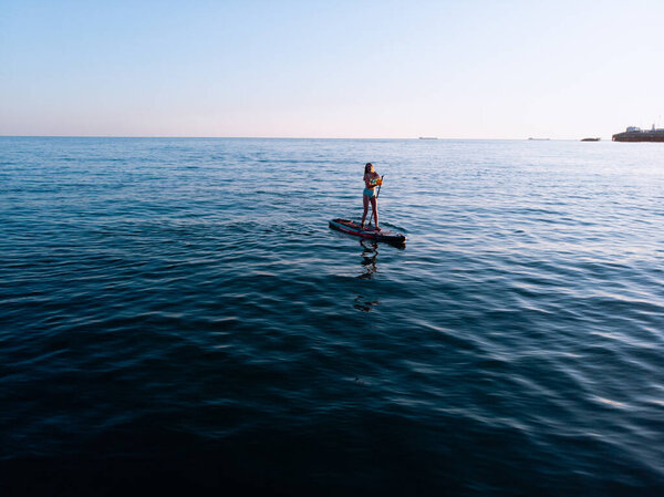 Attractive Woman on Stand Up Paddle Board, Woman paddling on sup board and enjoying turquoise transparent water. Tropical travel, wanderlust and water activity concept. Sunset and relax