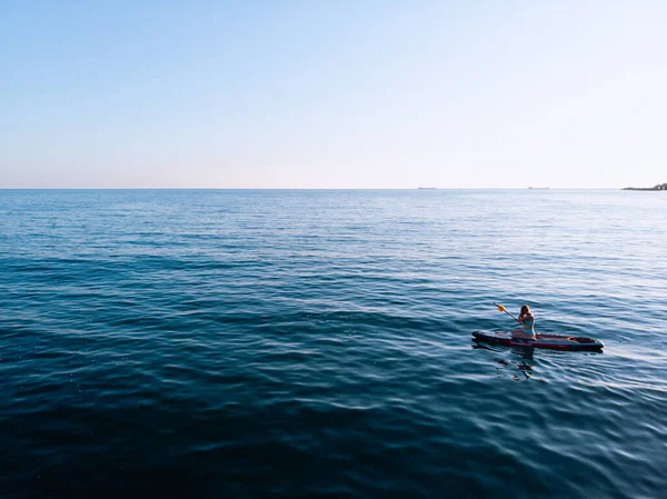 Stand Up Paddle tahtasında çekici bir kadın yemek masasında kürek çeken ve şeffaf suyun tadını çıkaran bir kadın. Tropik seyahat, seyahat tutkusu ve su aktivitesi konsepti. Gün batımı ve rahatlama