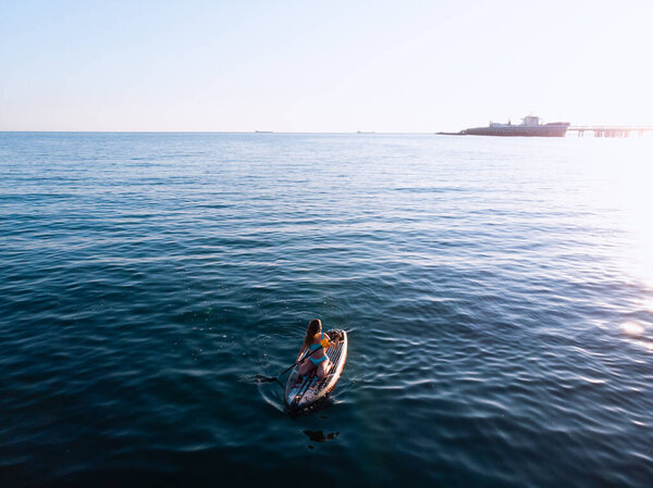 Attractive Woman on Stand Up Paddle Board, Woman paddling on sup board and enjoying turquoise transparent water. Tropical travel, wanderlust and water activity concept. Sunset and relax