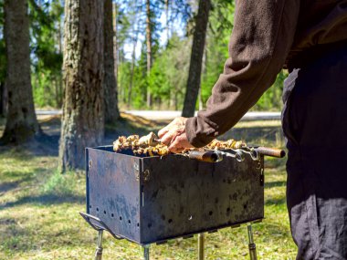 Barbeküyü ateşe veren adam. Arkaplanda orman. 