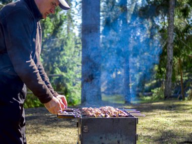 Yanan kömürün yanında ızgara yapmaya hazırlanan adam. Arka planda orman var. Barbekü ızgarası, barbekü.. 