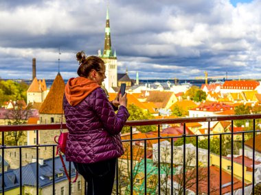 Kadın şehre doğru bakıyor ve akıllı telefonuyla eski kasabanın fotoğrafını çekiyor. Estonya 'da Turist