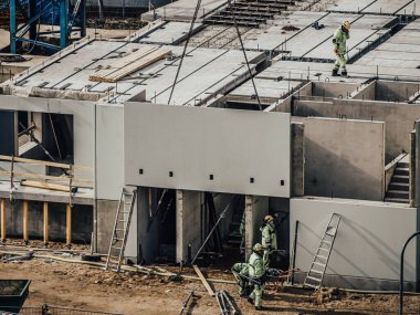Vinçli inşaatçılar çok katlı ev inşa ediyorlar. Kış ya da sonbahar arka planı. Apartman dairesinde vinçli işçiler. Mavi gökyüzünün altında. İş konsepti. Boşluğu kopyala. 