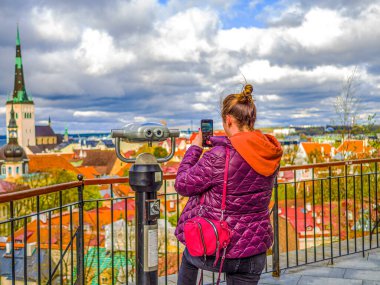 Kadın şehre doğru bakıyor ve akıllı telefonuyla eski kasabanın fotoğrafını çekiyor. Estonya 'da Turist