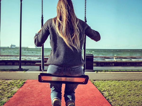 Estonya, Tallinn 'de güneşli bir günde okyanus sahilinde salıncakta sallanan genç bir kızın arka görüntüsü. 