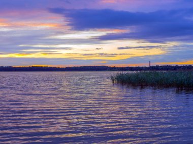 Akşam güneşinin panoramik manzarası. Yeşil ağaçlar, sis ve huzur yansıması. Estonya, Harku. Gölün üzerinde gün batımı