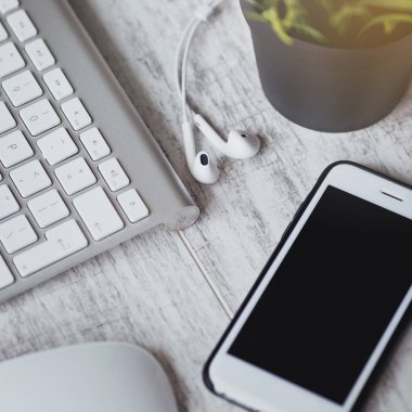 Şık çalışma alanı. Akıllı telefon ve kulaklık Beyaz ahşap masa üzerinde klavye ile. 