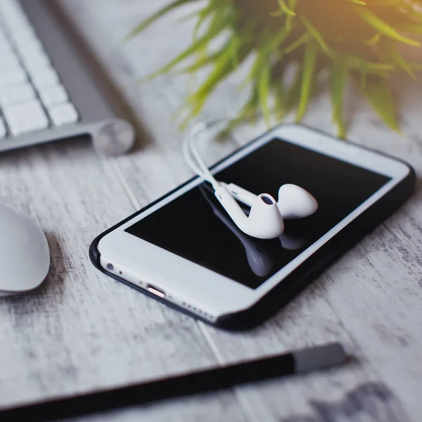 Stylish work space. Smartphone and earphone with keybord on the white wooden table.