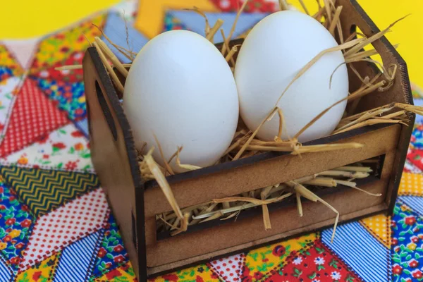 Sarı arka plana sahip bir patchwork kilim üzerinde tahta bir sandık içinde beyaz yumurta.