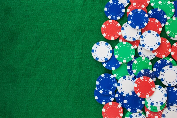 Colorful gambling chips on green felt background with copy space.