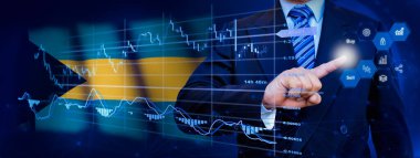 İş adamı KPI finansal grafikleri, sanal arayüzdeki stok ve pazarlama paneli ile veri analiz süreci sistemine dokunuyor. Arka planda Bahamalar bayrağı.