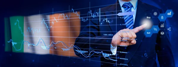 İş adamı KPI finansal grafikleri, sanal arayüzdeki stok ve pazarlama paneli ile veri analiz süreci sistemine dokunuyor. Arka planda İrlanda bayrağı.