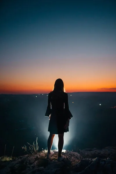 Gece şehrinin yukarısında genç bir kadının silueti