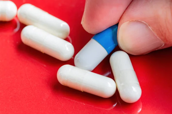 Fechar Dedos Pegando Uma Pílula Azul Branca Fundo Vermelho — Fotografia de Stock