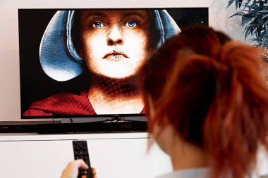 Benon, Fransa - 30 Aralık 2018: Kadın tutan bir Tv Uzaktan ve evlatlık'ın masalı izle. Evlatlık'ın hikaye fütüristik drama Tv serisi Bruce Miller tarafından oluşturulmuş