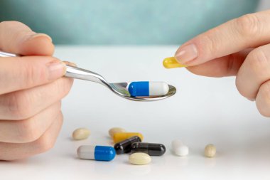 Portre renkli haplarla masanın altında bir kaşıkla kapsülündeymiş alarak genç kadın