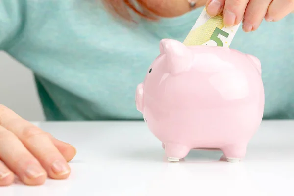 Woman Putting Bank note In Piggy Bank, Indoors