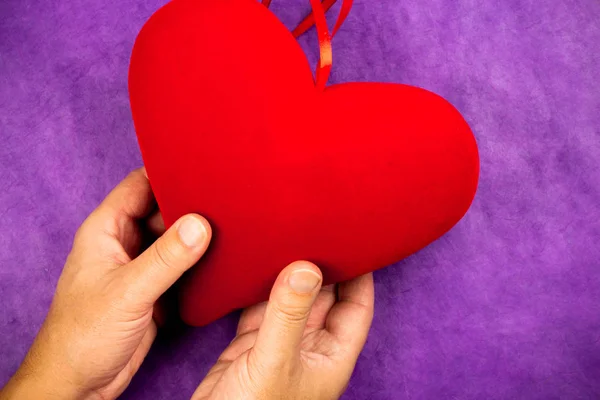 Mannens Hand Som Håller Ett Stort Rött Hjärta Lila Bakgrund — Stockfoto