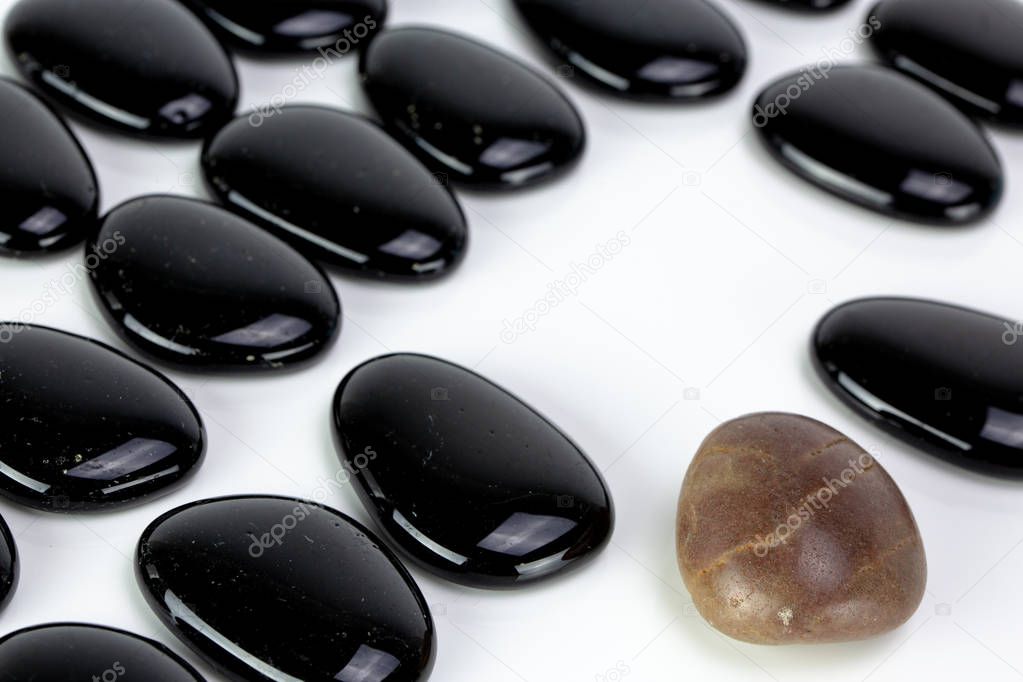 Black pebbles on white background with brown pebble. Concept of diversity or singularity