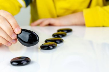 Beyaz bir tablo üzerinde siyah taşlarla oynayan çocuk