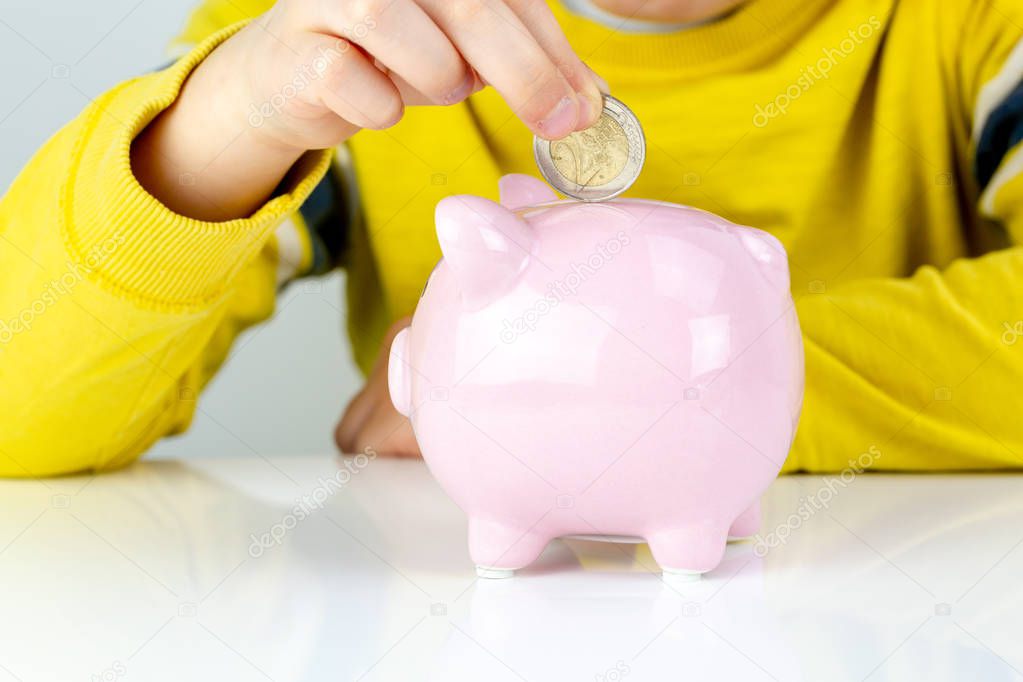 Seven years old boy puts money in a piggy bank, saving family concept