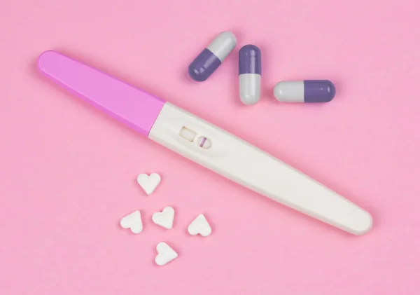 positive result on the pregnancy test with little hearts and pills over a pink background