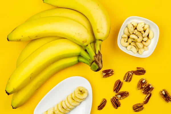 Raw Vegan breakfast: banana, nuts and berries on yellow background