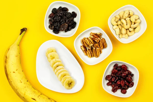 Raw Vegan breakfast: banana, nuts and berries on yellow background
