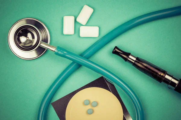 stethoscope and nicotine patch, chewin gum and ecigarette used for smoking cessation isolated on green background