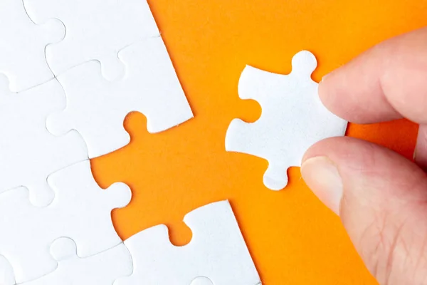 Hand hält ein weißes Puzzleteil auf orangefarbenem Hintergrund — Stockfoto