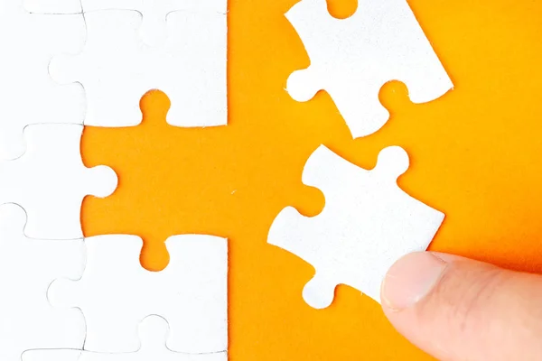 Hand hält ein weißes Puzzleteil auf orangefarbenem Hintergrund — Stockfoto