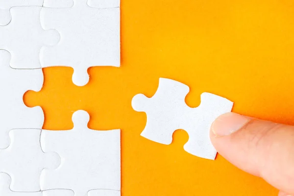 Hand hält ein weißes Puzzleteil auf orangefarbenem Hintergrund — Stockfoto