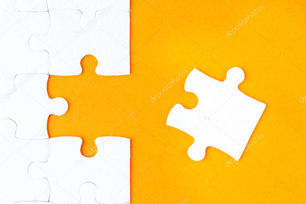 Hand holding piece of white puzzle on orange background. Business and team work concept.