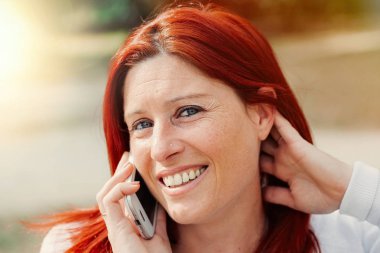Gülümseyen güzel genç kadın cep telefonu ile yakın, yaz yeşil park arka plan karşı.