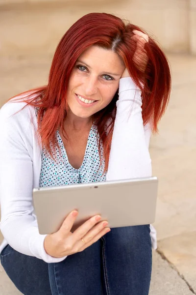 Портрет красивой рыжеволосой женщины с спокойным лицом и рукой в волосах с помощью планшета — стоковое фото