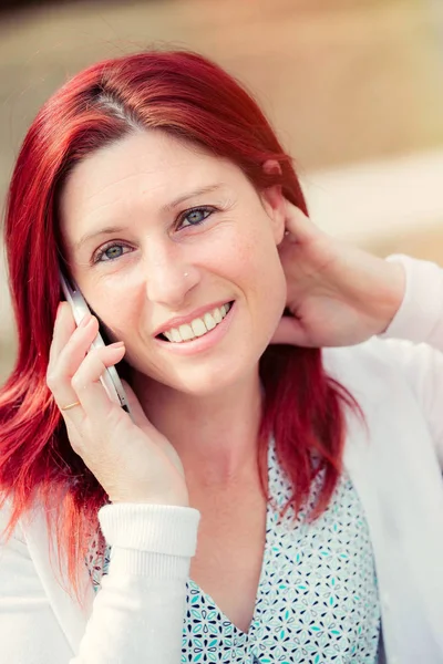 Sonriente hermosa joven sentada en un banco con teléfono móvil, contra el fondo del parque verde de verano . — Foto de Stock