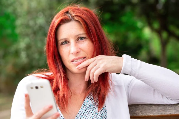 Sonriente hermosa joven de cerca con el teléfono móvil, sobre el fondo del parque verde de verano . — Foto de Stock