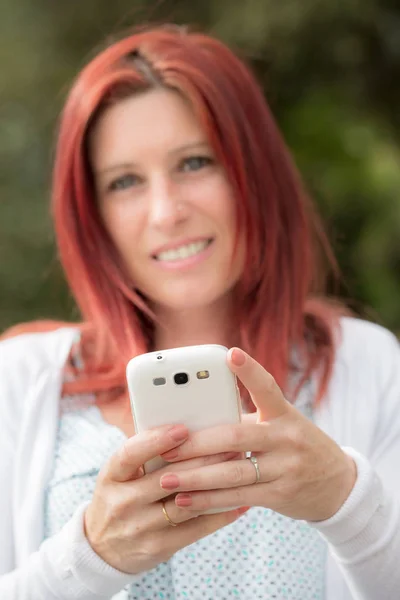 Sonriente hermosa joven de cerca con el teléfono móvil, sobre el fondo del parque verde de verano . — Foto de Stock